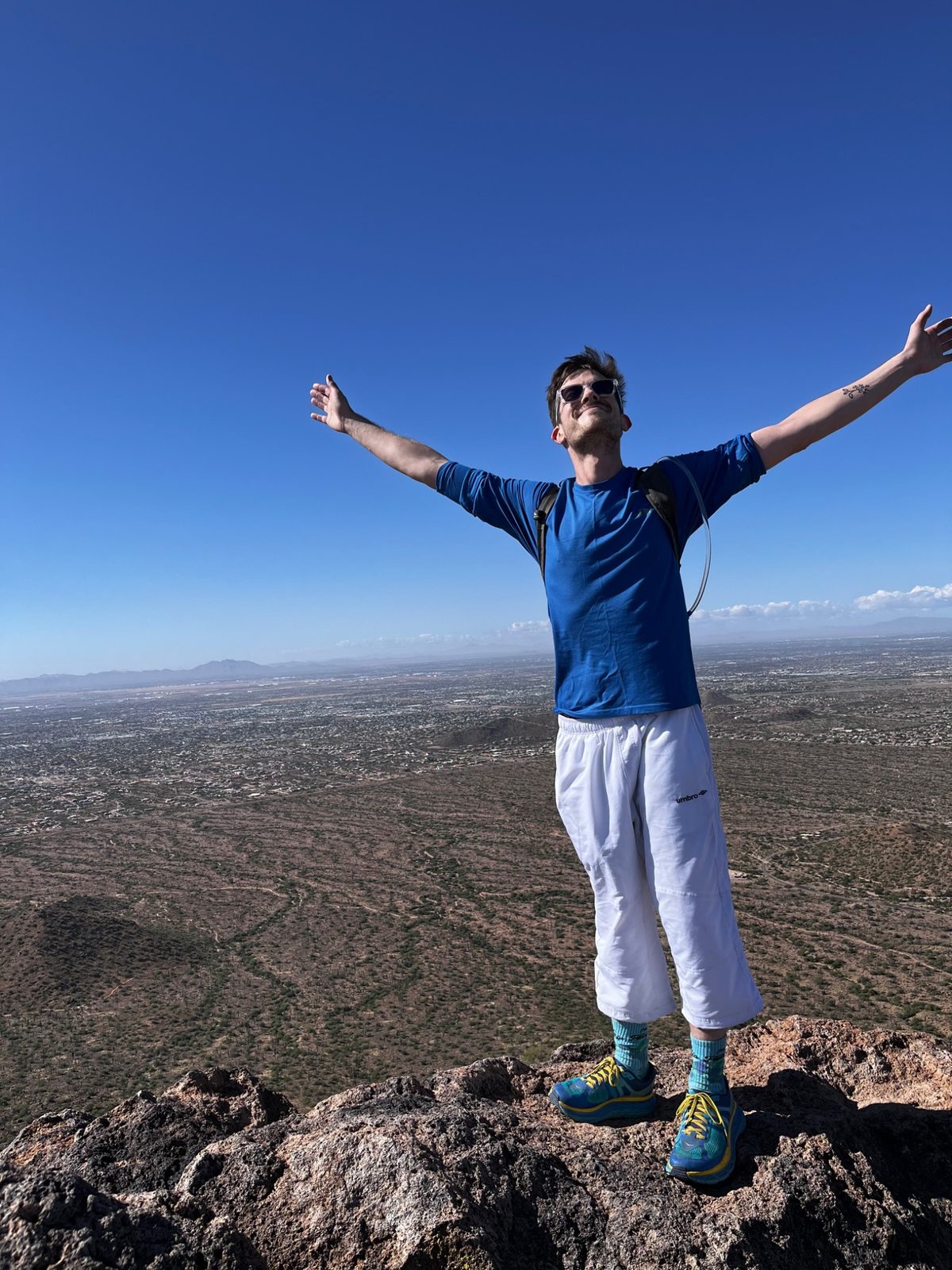 Brant standing on a mountaintop with arms raised — the journey of becoming a massage therapist